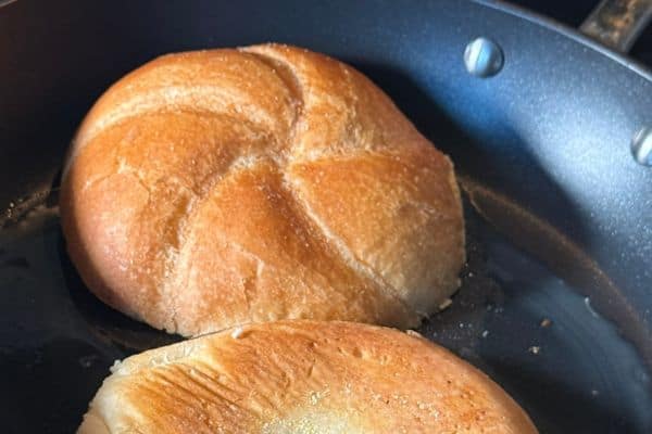 A hard roll toasting in a pan with butter