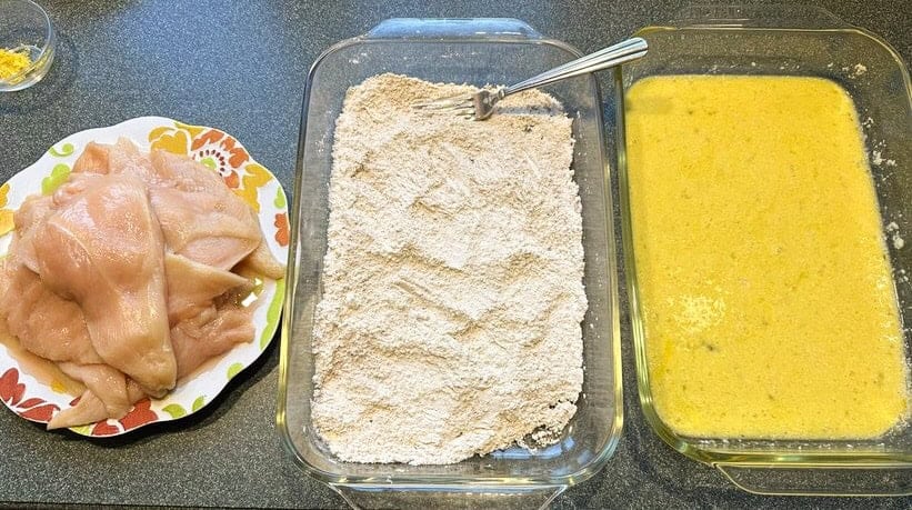 Dredging station for making Chicken Francese. A plate of chicken breast slices, one of flour, and one of egg mixture