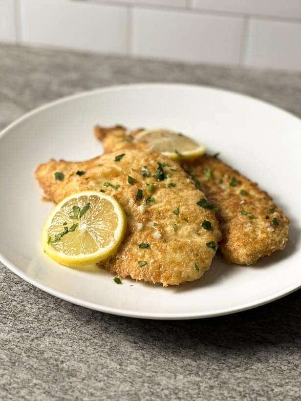 Chicken Francese on a white plate garnished with lemon slices