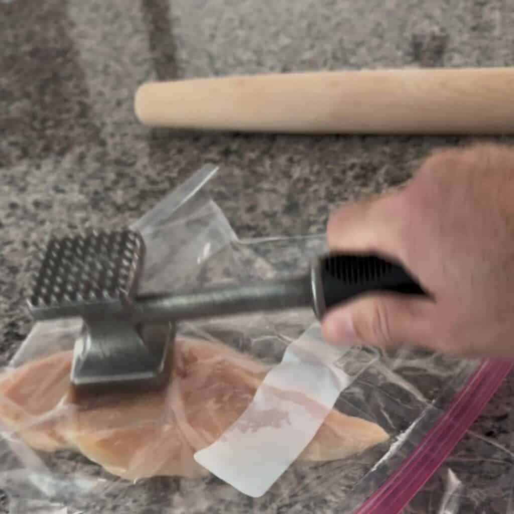 Demonstrating how to flatten chicken breast using a meat tenderizer