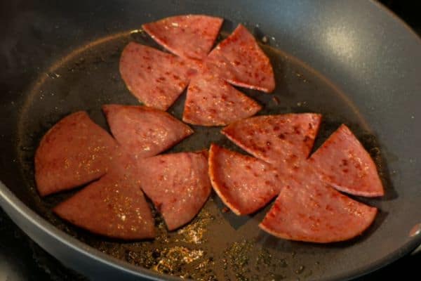 Three slices of taylor ham (pork roll) cooking in a pan