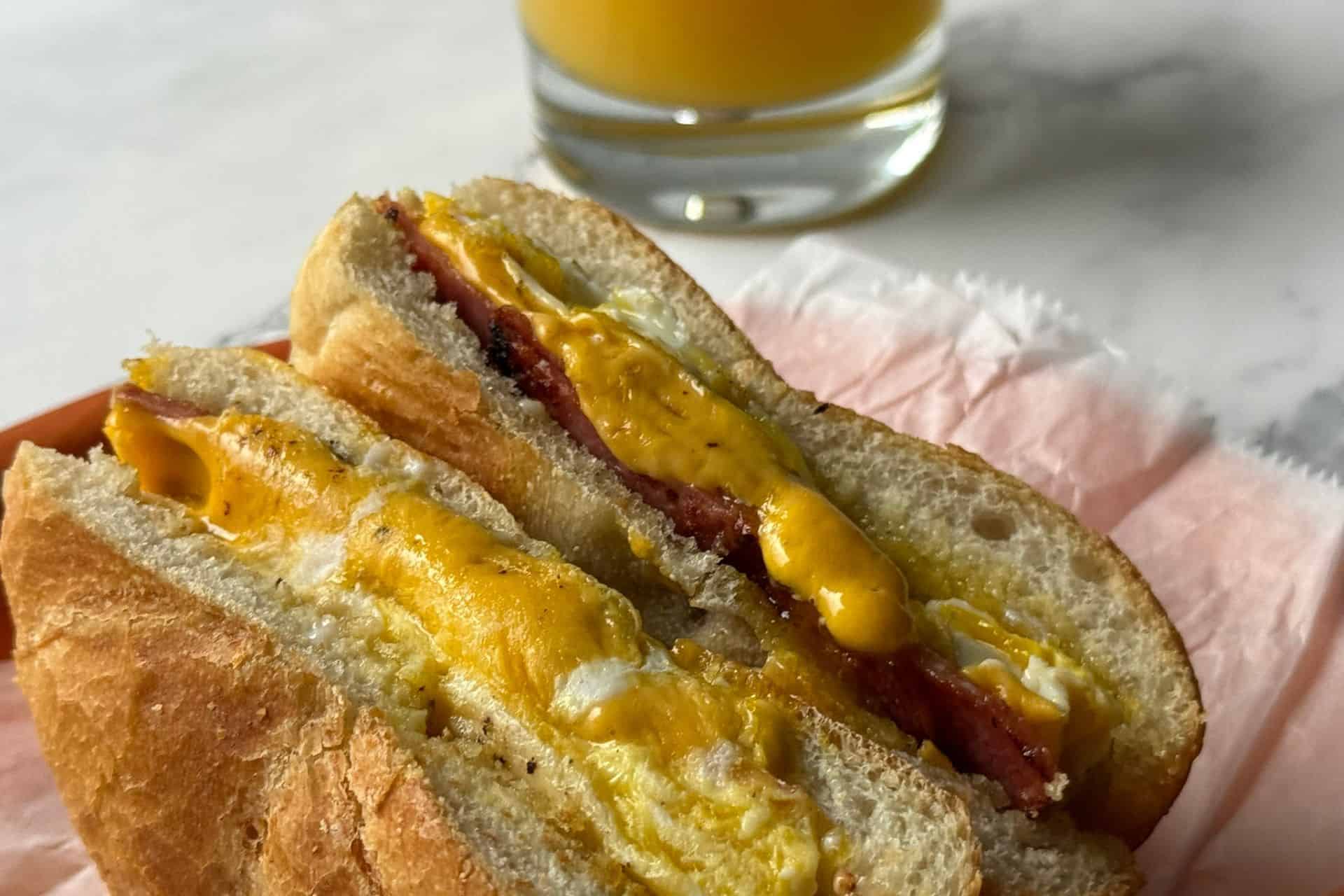 taylor ham, egg, and cheese sandwich on a plate with a glass of orange juice in the background