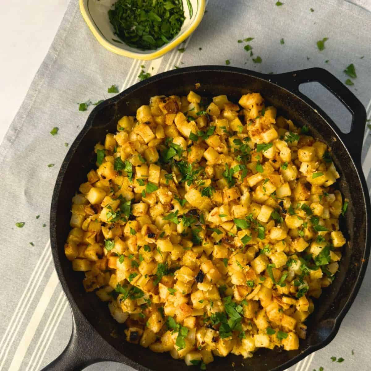 Cast iton pan full of crispy breakfast potatoes made with frozen hash browns