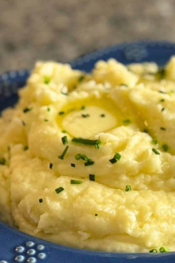 A blue bowl full of creamy garlic mashed potatoes garnished with chives