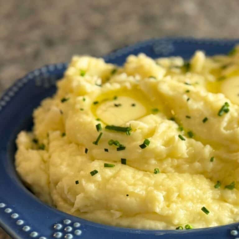 A blue bowl full of creamy garlic mashed potatoes garnished with chives