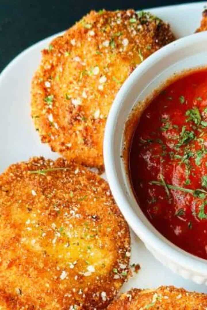 Italian fried ravioli on a white plate served with a small cup of marinara sauce