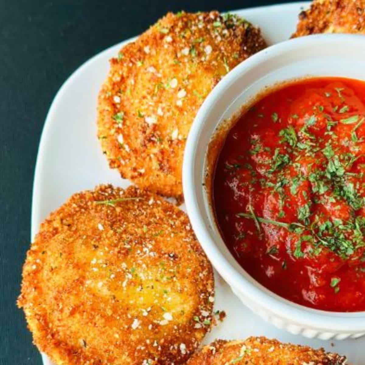 Italian fried ravioli on a white plate served with a small cup of marinara sauce