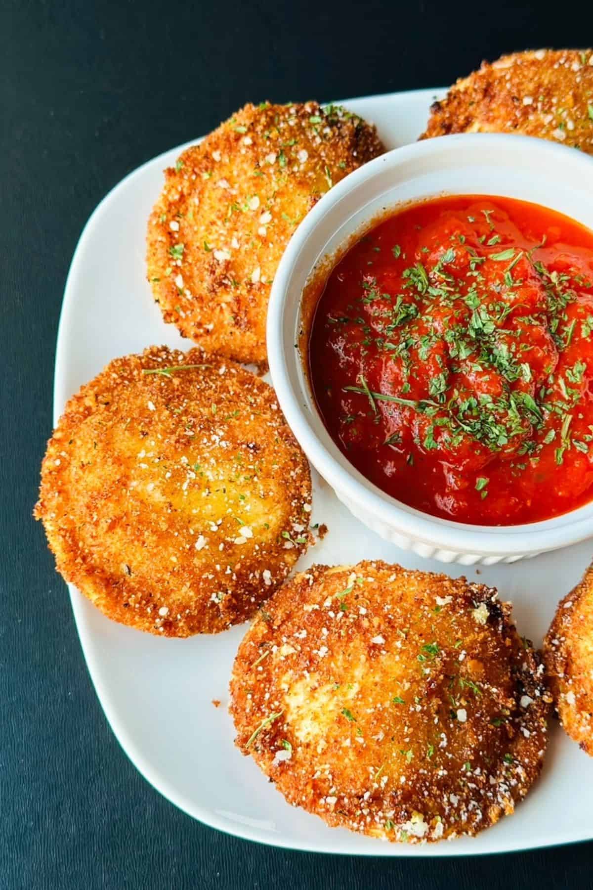 Italian fried ravioli on a white plate served with a small cup of marinara sauce