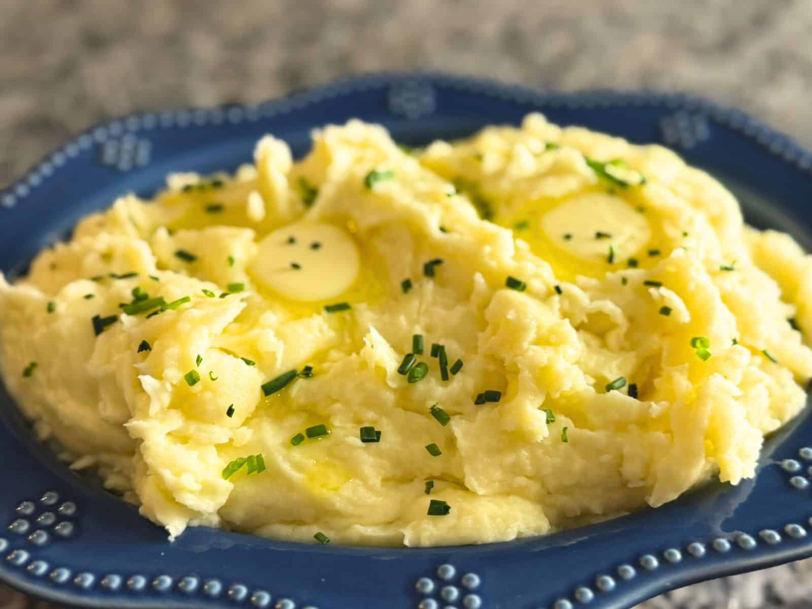 A blue bowl full of creamy garlic mashed potatoes garnished with chives