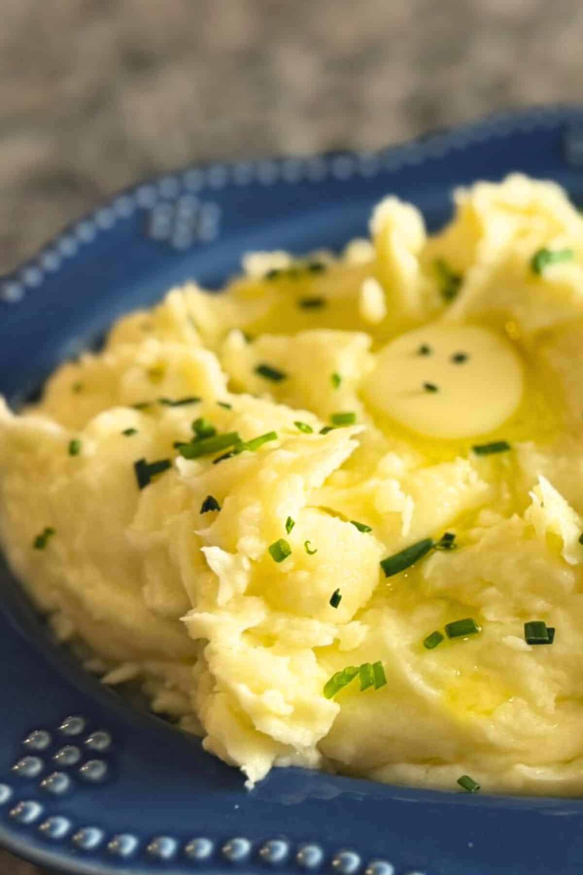 A blue bowl full of creamy garlic mashed potatoes garnished with chives