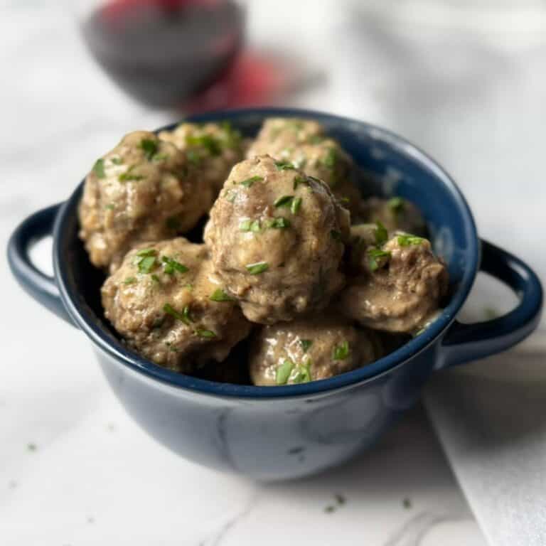 A blue bowl full of Swedish meatballs with a glass of red wine in the background