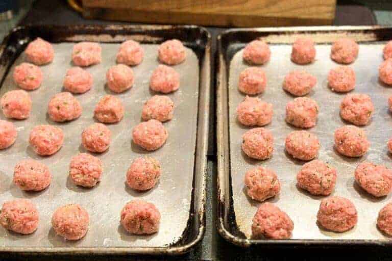 Two baking sheets full of raw Swedish meatballs about to go in the oven.