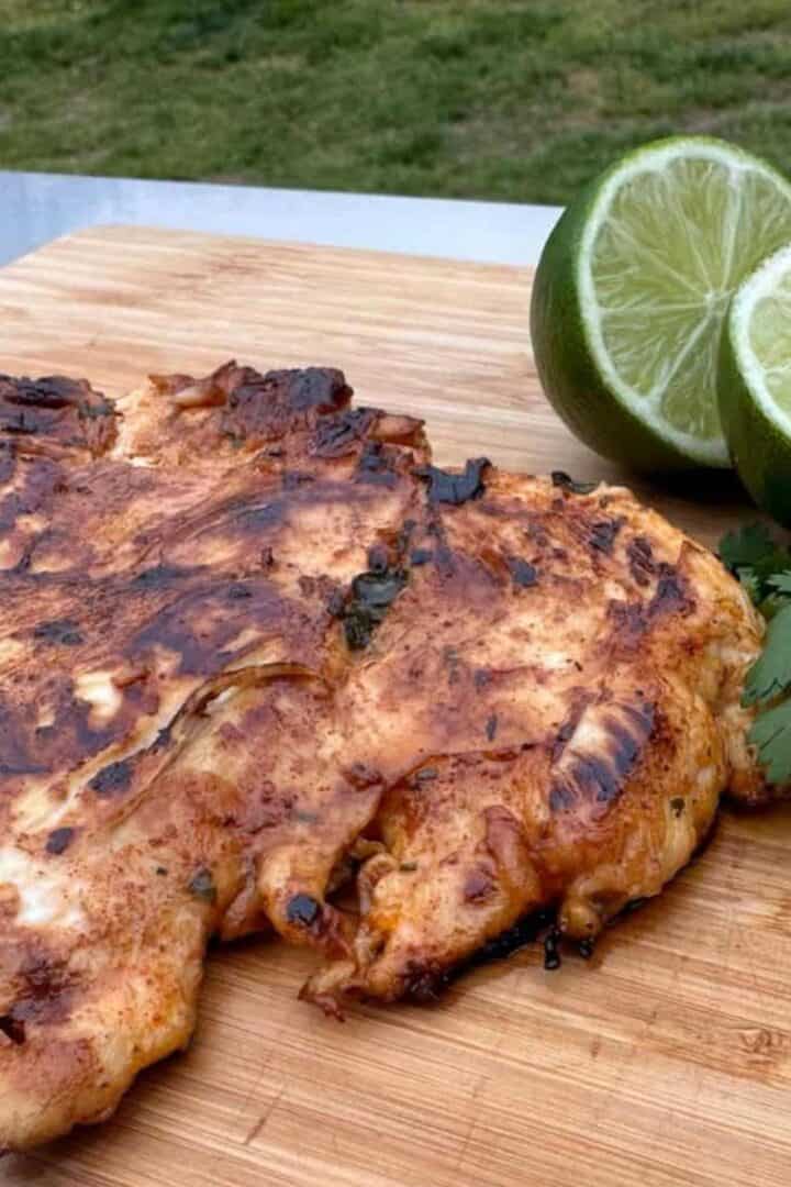 Piece of tequila lime chicken on a cutting board with lime slices, fresh cilantro, and a shot glass of tequila