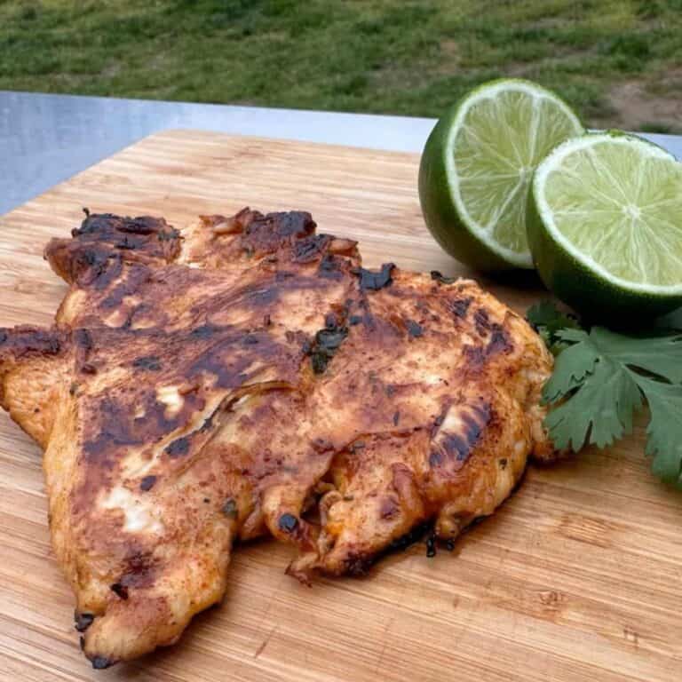 Piece of tequila lime chicken on a cutting board with lime slices, fresh cilantro, and a shot glass of tequila