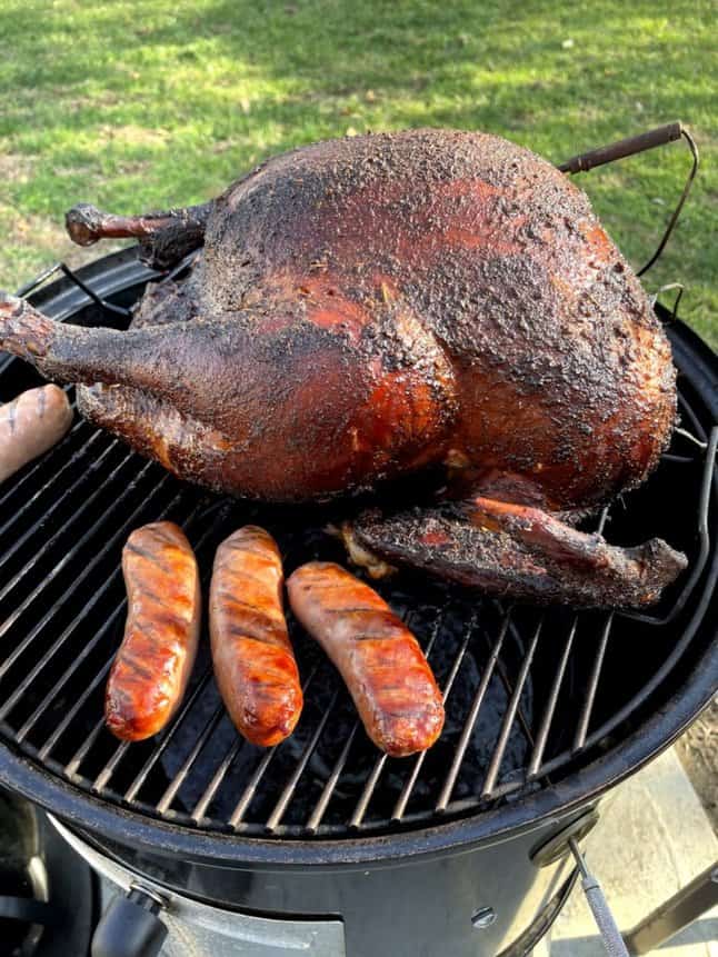 Turkey smoking on a charcoal smoker with some sausage links