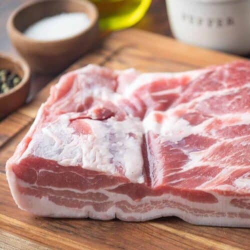 Thick slab of pork belly on a wooden cutting board