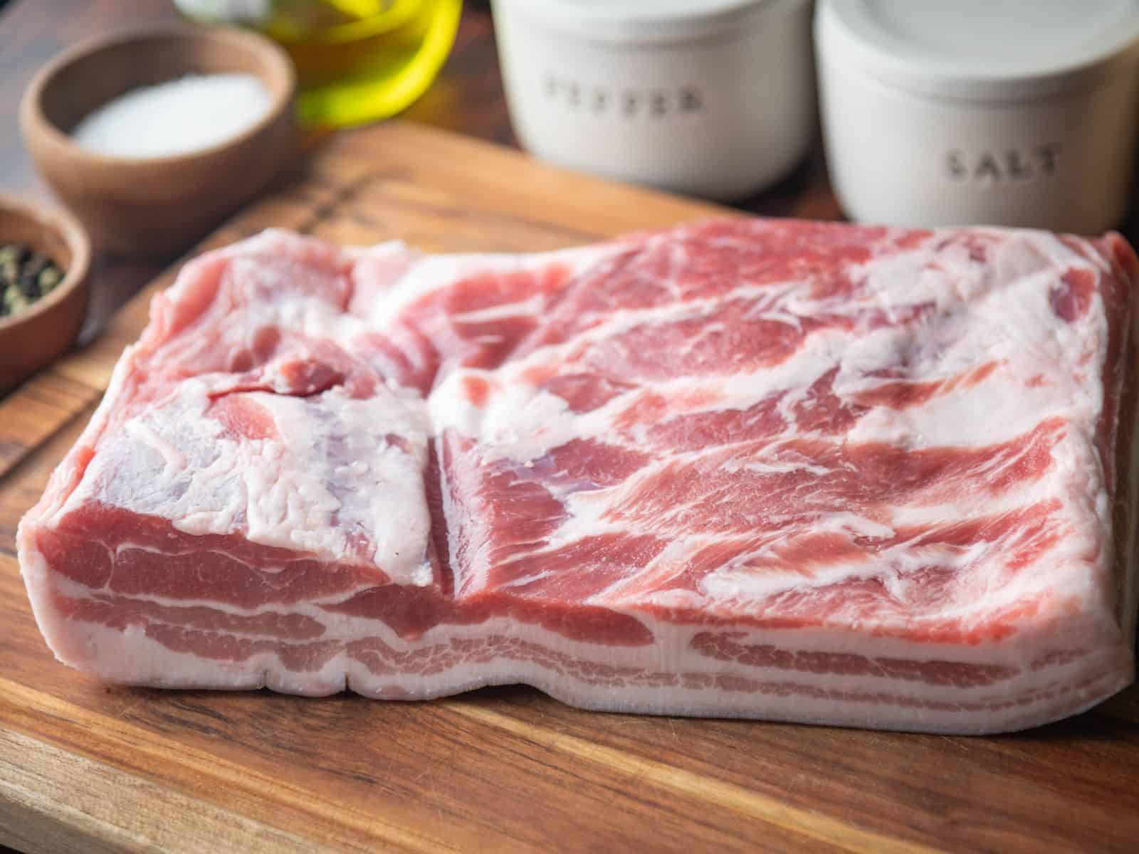 Thick slab of pork belly on a wooden cutting board