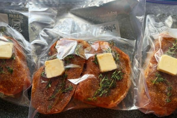 Four pork chops seasoned with dry rub and topped with fresh thyme and butter and placed in a plastic bag before being cooked sous vide