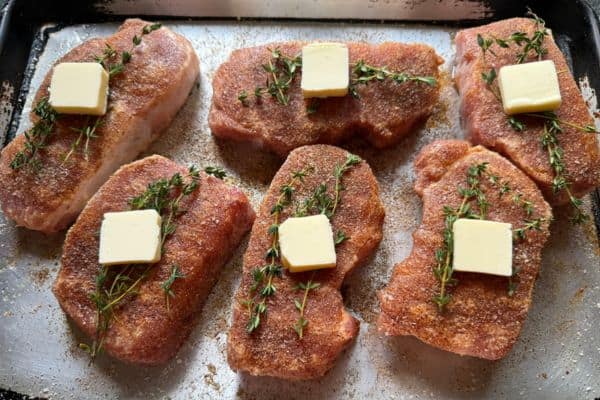 Six pork chops seasoned with dry rub and topped with fresh thyme and butter