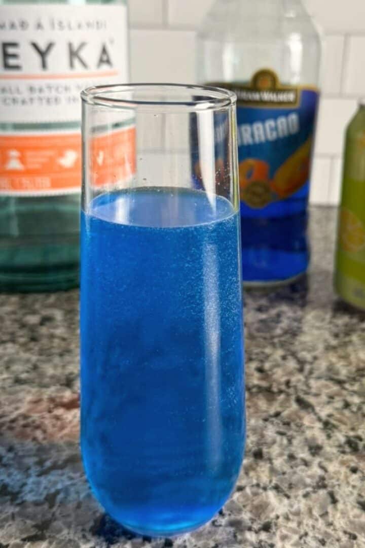 A Star Trek inspired glass of bright blue "Romulan Ale" and the ingredients lined up behind it