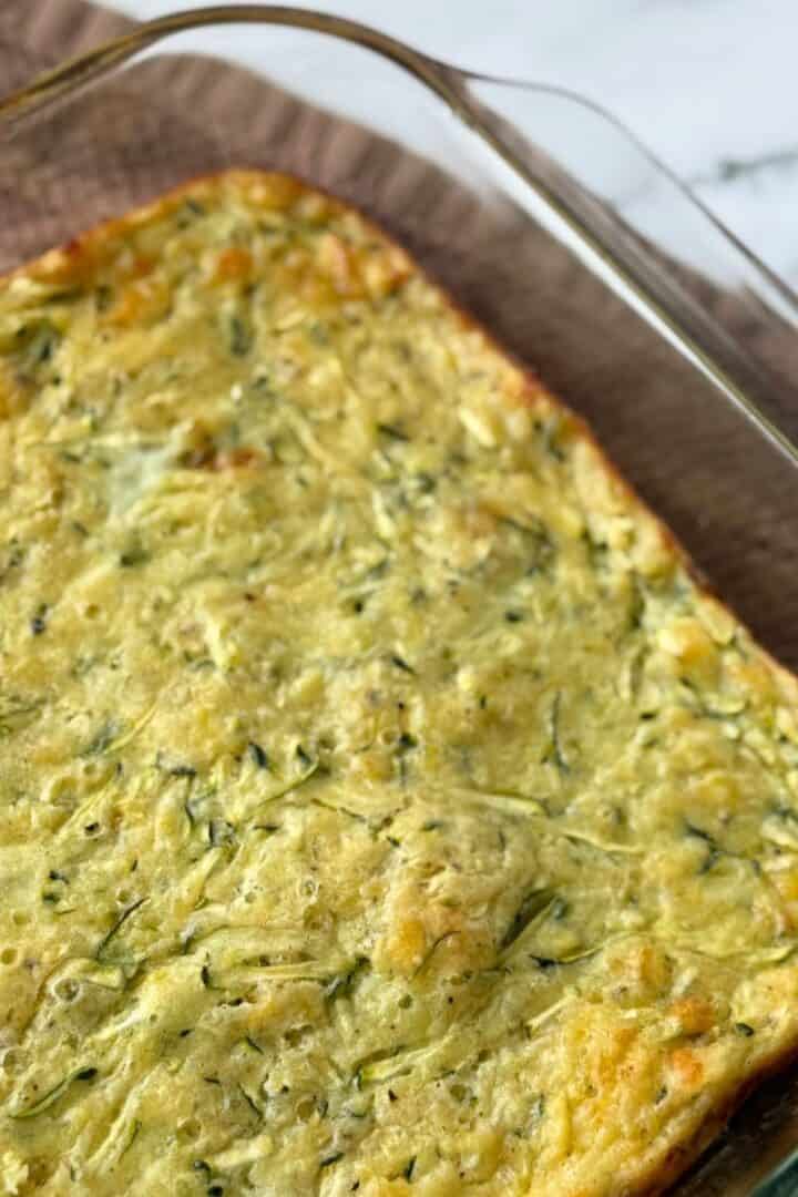 A baked zucchini pie fresh out of the oven and cooling in a glass baking dish