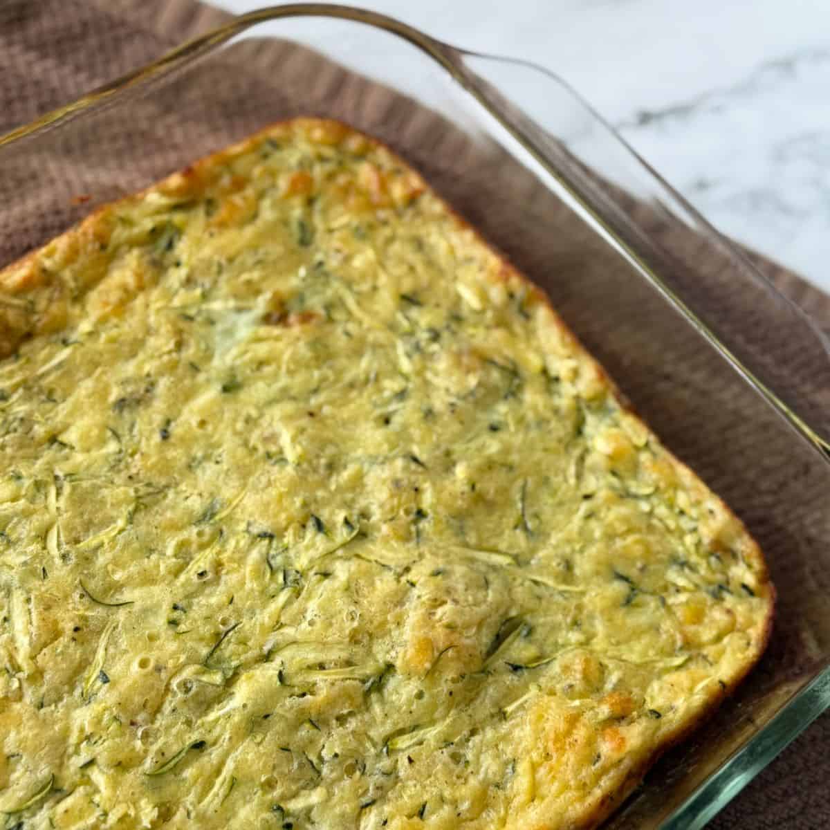 A baked zucchini pie fresh out of the oven and cooling in a glass baking dish