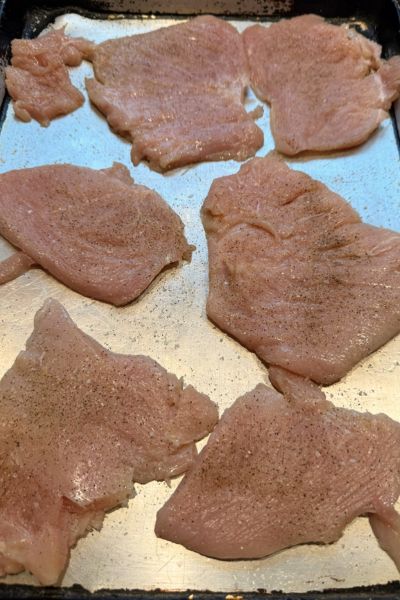 Seasoned chicken breast cutlets on a metal baking sheet pan
