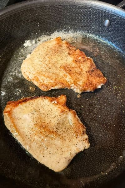 Two chicken cutlets frying in oil and butter