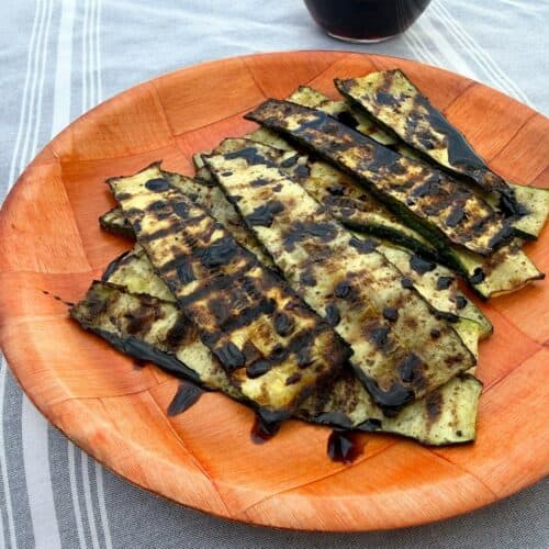 Grilled zucchini on a wooden plate and drizzled with balsamic glaze
