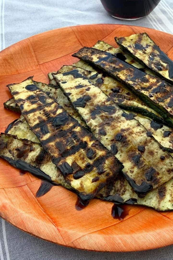 Grilled zucchini on a wooden plate and drizzled with balsamic glaze
