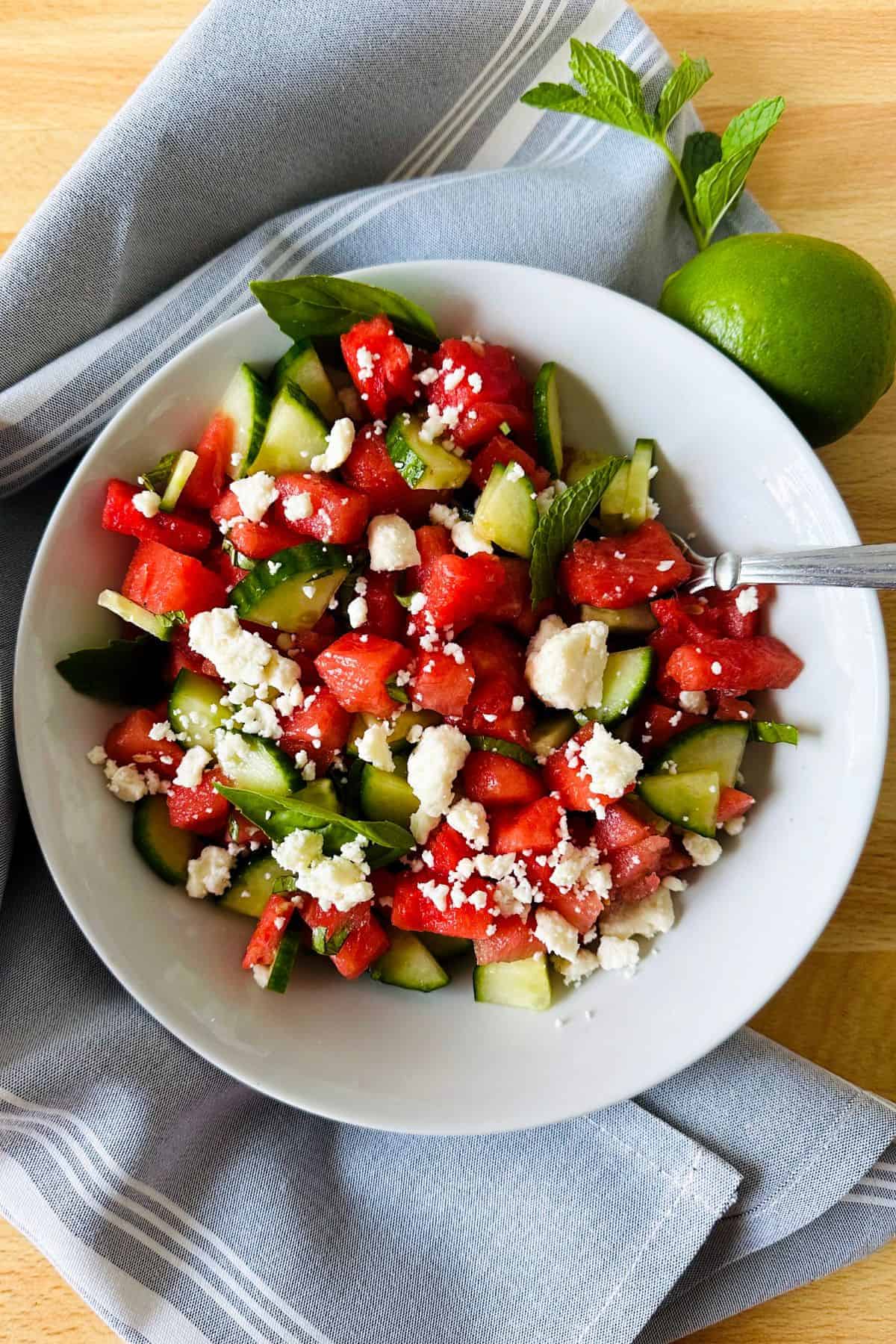 White bowl of watermelon feta mint salad garnished with a fresh lime
