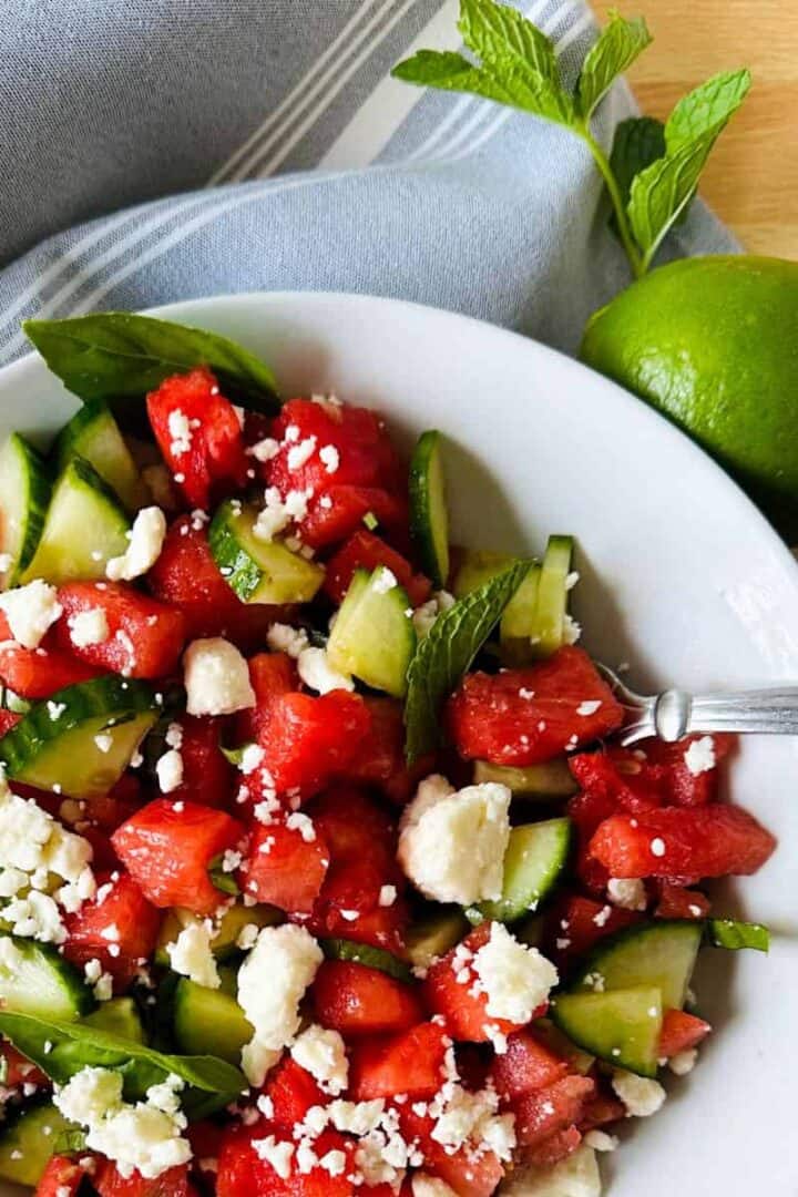 White bowl of watermelon feta mint salad garnished with a fresh lime