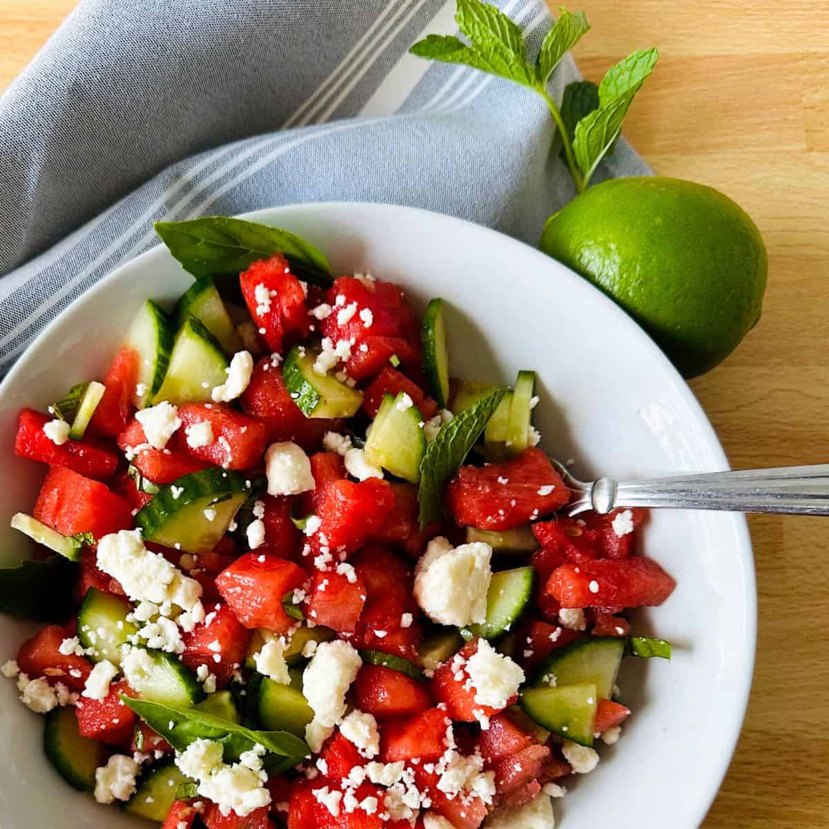 White bowl of watermelon feta mint salad garnished with a fresh lime