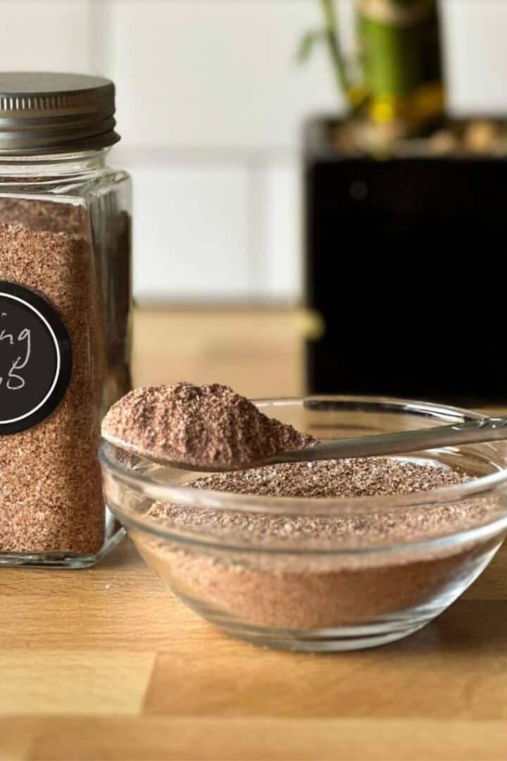 A jar of homemade chicken win g dry rub, also a glass bowl full of it and a small spoon resting on the bowl
