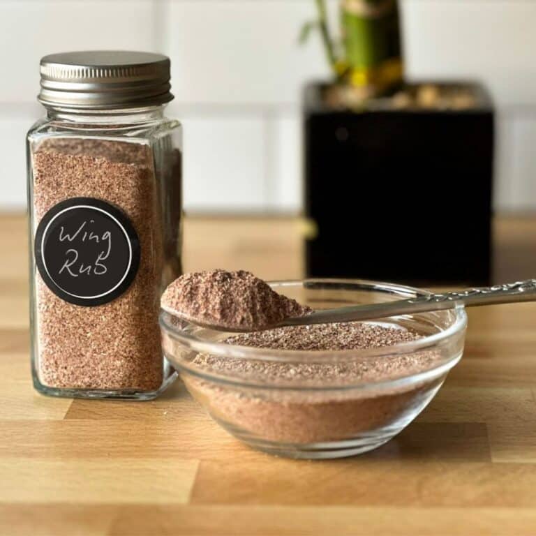 A jar of homemade chicken win g dry rub, also a glass bowl full of it and a small spoon resting on the bowl