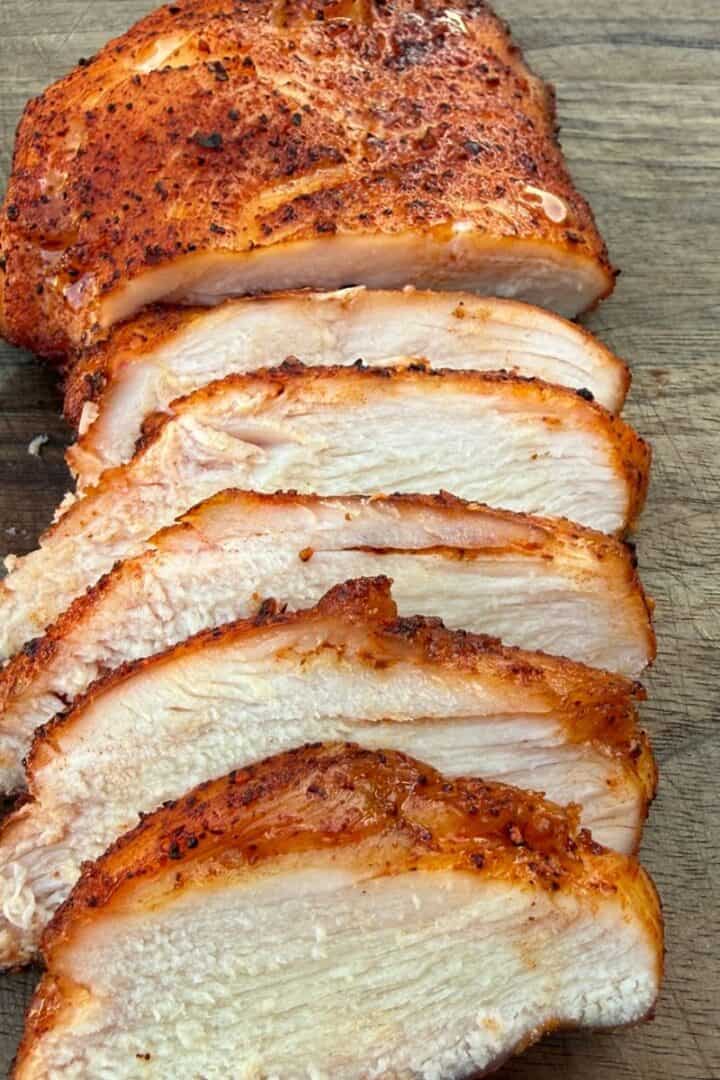 A smoked chicken breast sliced on a wood cutting board