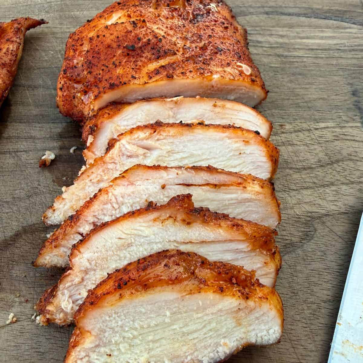 A smoked chicken breast sliced on a wood cutting board