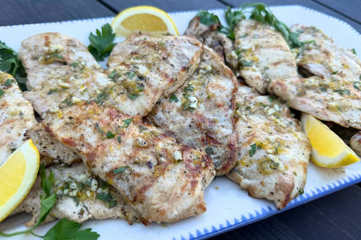 Slices of marinated grilled chicken cutlets on a platter and garnished with fresh parsley and lemon slices