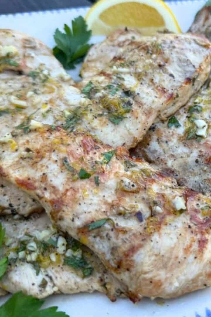 Slices of marinated grilled chicken cutlets on a platter and garnished with fresh parsley and lemon slices