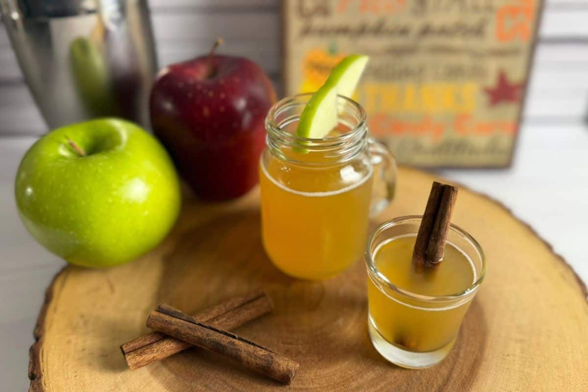 Two glasses of caramel apple pie shot garnished with apple slices and cinnamon sticks