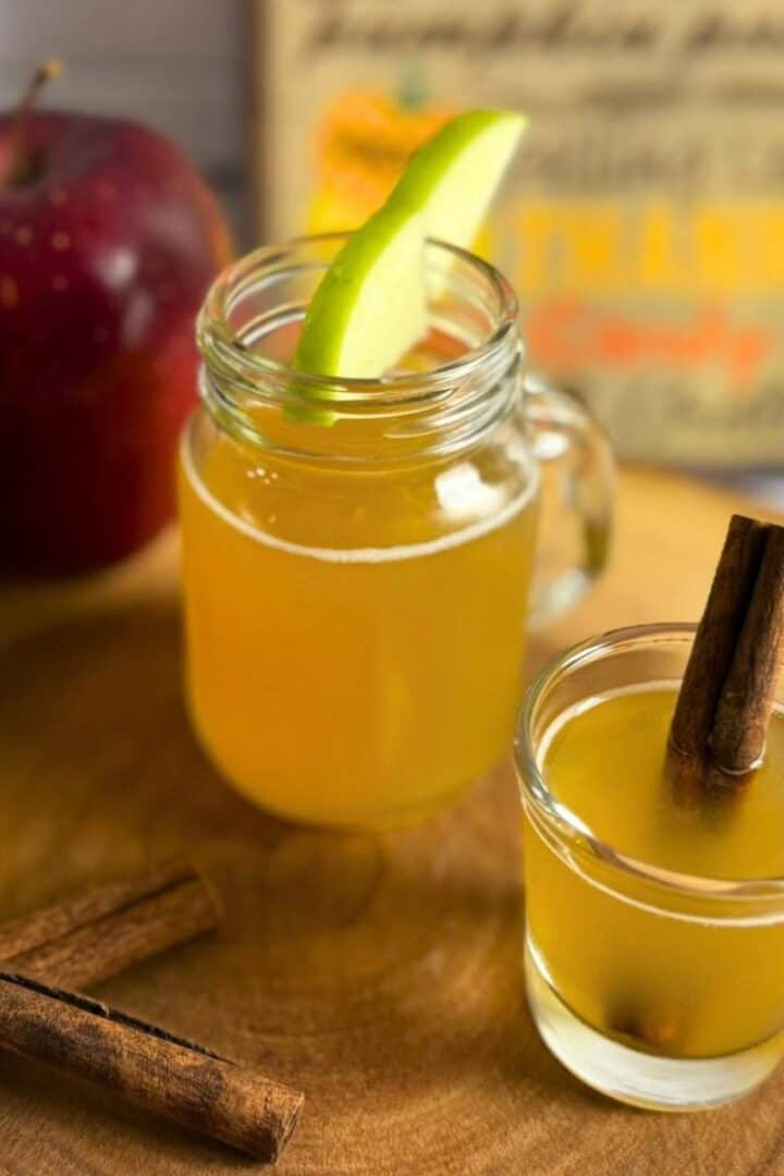 Two glasses of caramel apple pie shot garnished with apple slices and cinnamon sticks