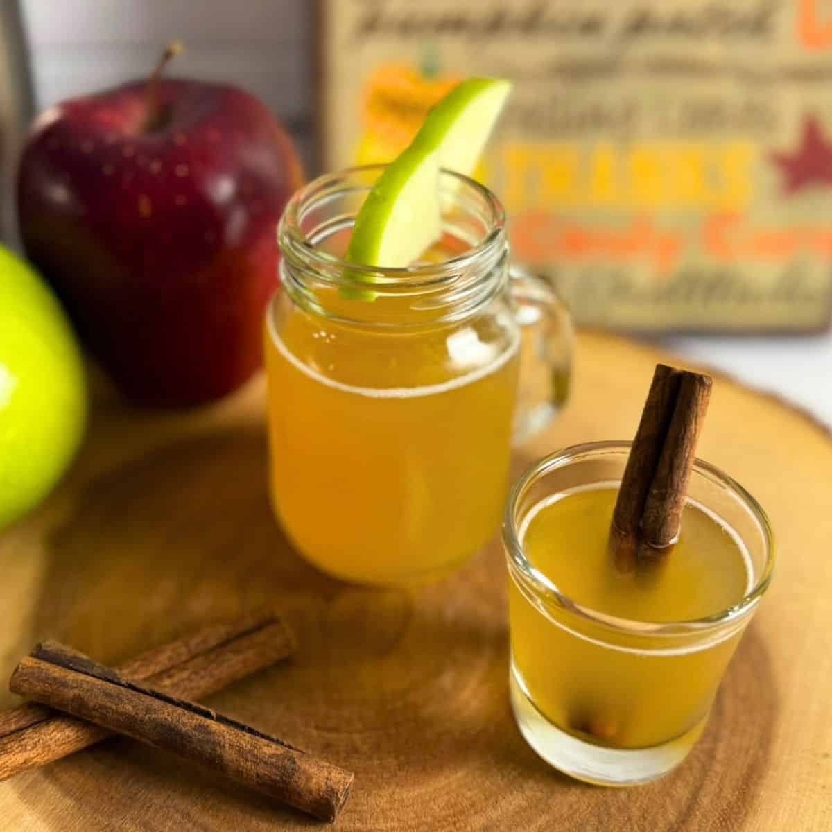 Two glasses of caramel apple pie shot garnished with apple slices and cinnamon sticks